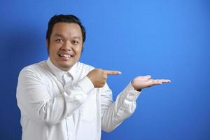 Portrait of Asian young happy office worker smiling and pointing to presenting something on his side photo