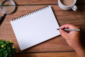 Wooden table with notebook, magnifying glass, pen, decorative plants photo