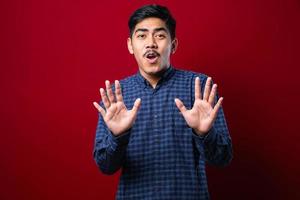 Young handsome asian man wearing casual shirt standing over moving away hands palms showing refusal and denial with afraid and disgusting expression. Stop and forbidden. photo