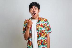 Asian man in white tshirt smiling and pointing to presenting something on his side, against red background with copy space photo