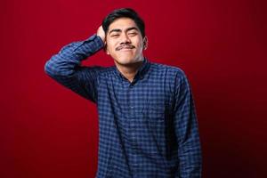 Young handsome man with mustache wearing casual shirt standing over red background confuse and wonder about question. photo