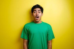 cara sorprendida de un hombre asiático con una camiseta verde de fondo amarillo foto