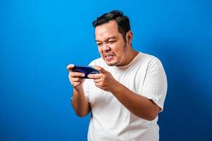 Angry Fat Asian Guy Playing Games on Tablet Smart Phone against blue background photo