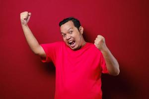 Young asian man happy and excited expressing winning gesture. Successful and celebrating over red background photo