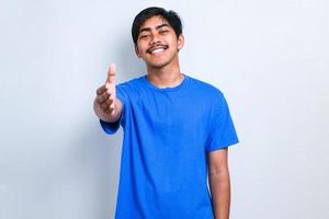Asian young man wearing casual clothes smiling friendly offering handshake as greeting and welcoming photo