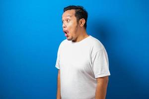 Fat Asian man in white t-shirt shows funny shocked and surprise expression against blue background photo