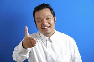 Portrait of young Asian man offering handshake and smiling against blue background photo