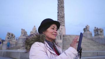 mujer asiática feliz de pie y tomando una foto en un teléfono inteligente en el parque vigeland, noruega. hermoso día con hermosas esculturas y cielo azul, oslo video