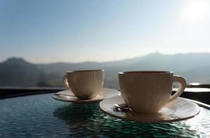 foto de dos tazas de café en la mesa con vistas a la montaña por la mañana. pareja juntos y concepto de relación