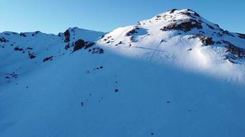 vista aerea, drone di alpinista solista che cammina, fa escursioni in una giornata di sole invernale per raggiungere la vetta della montagna. viaggiare e entrare in contatto con la natura. raggiungere la vetta della montagna. camminare sulla neve profonda. video