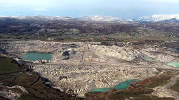 Aerial view of working mine pit. Drone shot of coal mining activity. Artificial polluted lakes. Mountains with snow in the background. Extraction. Machine working. Destroyed landscape. video