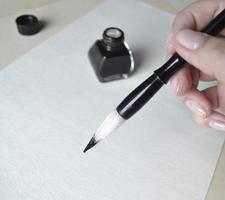 botella de tinta con pincel en la mano para dibujar pintura china en blanco foto