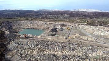 vista aérea del pozo de la mina en funcionamiento. toma de drones de la actividad minera del carbón. lagos artificiales contaminados. montañas con nieve en el fondo. extracción. funcionamiento de la máquina. paisaje destruido. video