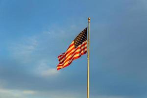American flag on flagpole waving in the wind against clouds, blue sky photo