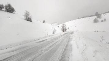 camino helado en un día de invierno. fuerte ventisca y nieve que cae en una zona montañosa. carreteras cubiertas de nieve. cuidado al conducir. vientos fuertes.