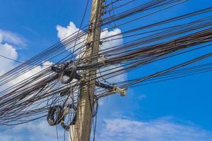 Absolute cable chaos on Thai power pole Thailand blue sky. photo
