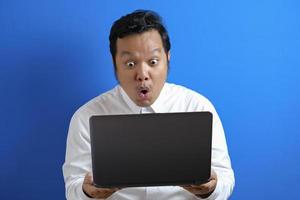 Young Asian businessman wearing casual white shirt looking at laptop, surprised expression. photo