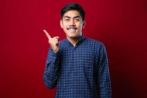 Young handsome asian man wearing casual shirt with a big smile on face, pointing with hand finger to the side looking at the camera. photo
