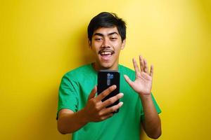 Asian man taking selfie photo or doing a video call at home, smiling to camera and waving