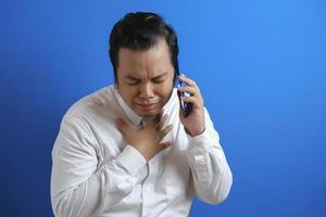 a photo of an asian man in an office worker looking sad over the news he received on his smart phone