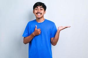 hombre asiático con camisa informal con una gran sonrisa en la cara, señalando con el dedo de la mano hacia un lado mirando la cámara. foto