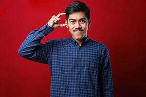 Young handsome man wearing casual shirt smiling and confident gesturing with hand doing small size sign with fingers looking and the camera. measure concept. photo