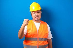 trabajador de la construcción asiático hombre vestido con chaleco naranja y casco de seguridad con puño cerrado foto