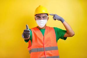 Asian construction worker pointing at his protective mask and savety helmet photo