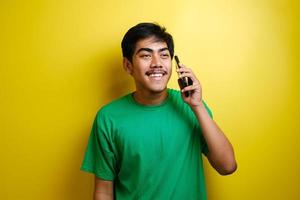 Cheerful young asian man on call against yellow background photo