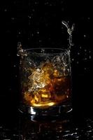 glass of scotch whiskey with splash and ice on black background photo