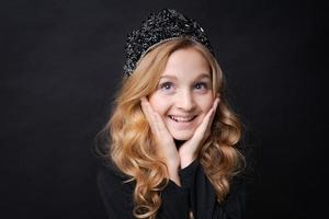 Children's portrait cute girl with crown on her head folded her hands near her photo