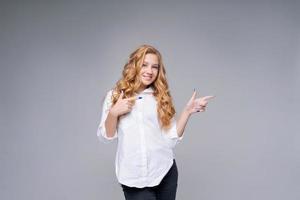 Reliable cheerful girl in white shirt points her finger at an empty space photo