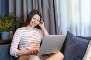 Young woman sitting on couch, working at laptop, browsing internet or reading photo