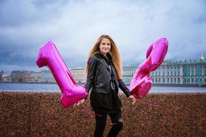 niña feliz sosteniendo globos en el terraplén de la ciudad en una chaqueta de cuero. foto