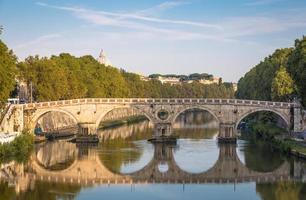 Bridge on Tiber river in Rome, Italy. Vatican Basilica cupola in background with sunrise light. photo