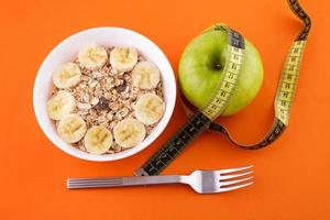 muesli with banana on orange background with apple and measuring tape photo