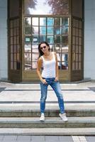 Cute woman in sunglasses poses on the steps in the street near the building photo