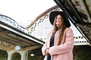 bella joven con sombrero negro y abrigo rosa con soportes para maletas foto