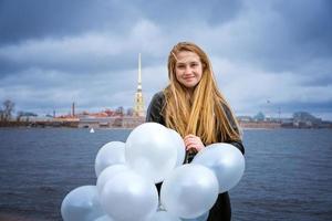 Happy cheerful girl having fun with big white latex balloons. Outdoors on the photo