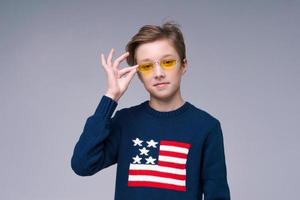 hombre europeo feliz con gafas amarillas y suéter azul con bandera estadounidense en gris foto