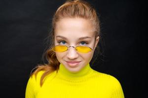 Close-up portrait happy young girl with blond hair, looks through yellow photo