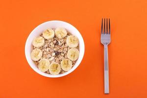 oatmeal in a plate with a banana and a fork on an orange background photo