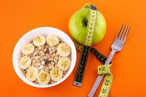 muesli con plátano sobre fondo naranja con manzana y cinta métrica foto