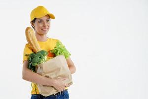 mujer de entrega sonriente en amarillo posando con bolsa de supermercado, fondo blanco foto