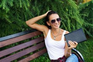 Photo of young beautiful woman sitting on wooden bench in park with black