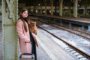 hermosa joven turista casual con perro y maleta esperando el tren foto