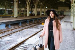 Young woman with suitcase on platform of station. Traveler girl waiting