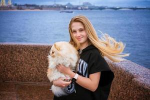 alegre y feliz niña adolescente sostiene y abraza a pomeranian spitz en el terraplén foto