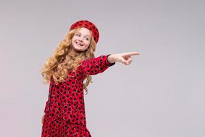 Little girl in french style hat points her finger to side. Happy girl with long photo