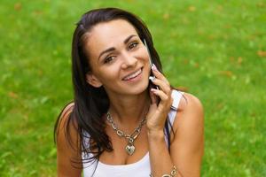 retrato de una hermosa chica caucásica. estudiante sonriente se sienta en la hierba verde foto